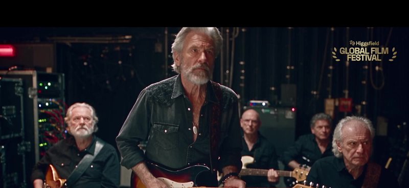 Adam HIL, silver hair and beard, plays a sunburst Fender in a dark shirt, backed by his band of veteran musicians among road cases.